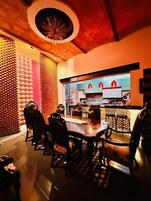 Un comedor con una mesa redonda y sillas, una cocina al fondo y un muro con diseño.