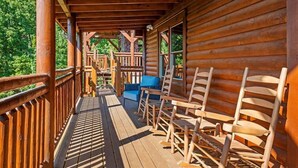 A wooden cabin with a porch, wooden chairs, and a bench. - Sleeps ~22, Heated Indoor Pool, Hot Tub, Game Room (Sevierville)