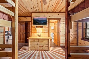 A log cabin interior with a wooden bench, a mounted television, and a striped rug. - Sleeps ~22, Heated Indoor Pool, Hot Tub, Game Room (Sevierville)