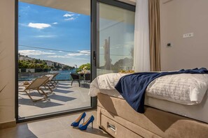 A bedroom with a bed, a glass door leading to a balcony with a pool and chairs, and a pair of shoes on the floor. - Villa Between Seas with Pool (Ražanj)