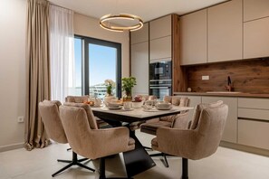 A modern dining area with a round table, six chairs, and a view of the city. - Villa Between Seas with Pool (Ražanj)