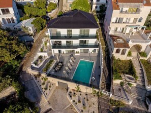 A modern two-story house with a rooftop pool, surrounded by greenery and adjacent to other buildings. - Villa Between Seas with Pool (Ražanj)