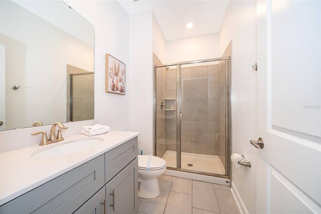 Une salle de bain moderne avec une douche à parois de verre, un lavabo blanc avec un robinet doré et un grand miroir.