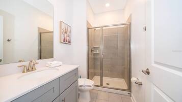 Une salle de bain moderne avec une douche à parois de verre, un lavabo blanc avec un robinet doré et un grand miroir.