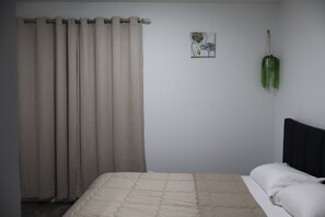 Ein Schlafzimmer mit Bett, Vorhängen, einer Wandpflanze und einem kleinen Gemälde.