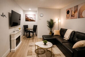 Ein modernes Wohnzimmer mit Flachbildfernseher, Kamin, Essbereich mit Stühlen, Sofa und Couchtisch.