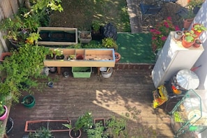 Eine Holzterrasse mit erhöhten Blumenbeeten, Topfpflanzen und einem kleinen Tisch.
