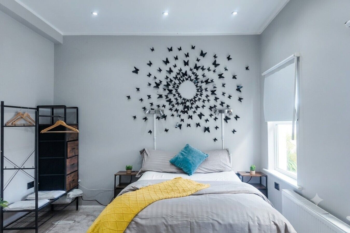 A bedroom with a bed, a wardrobe, a wall-mounted butterfly decoration, a window, and a radiator.