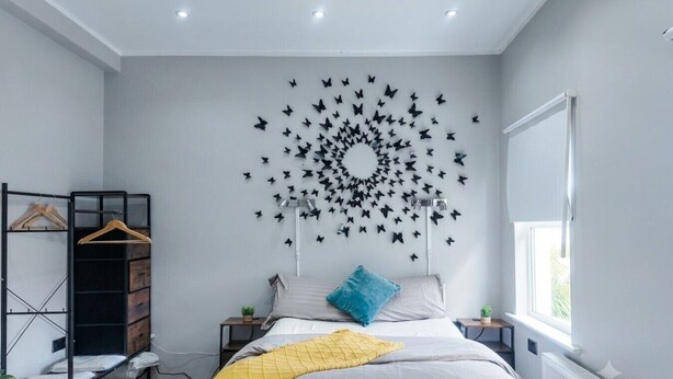 A bedroom with a bed, a wardrobe, a wall-mounted butterfly decoration, a window, and a radiator. - London Southeast Modern Stay (London)