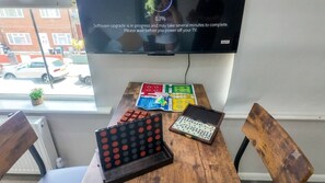 Ein Zimmer mit Fernseher, der eine Software-Aktualisierung anzeigt, einem Holztisch mit Gesellschaftsspielen und einem Fenster mit Blick auf eine Straße.