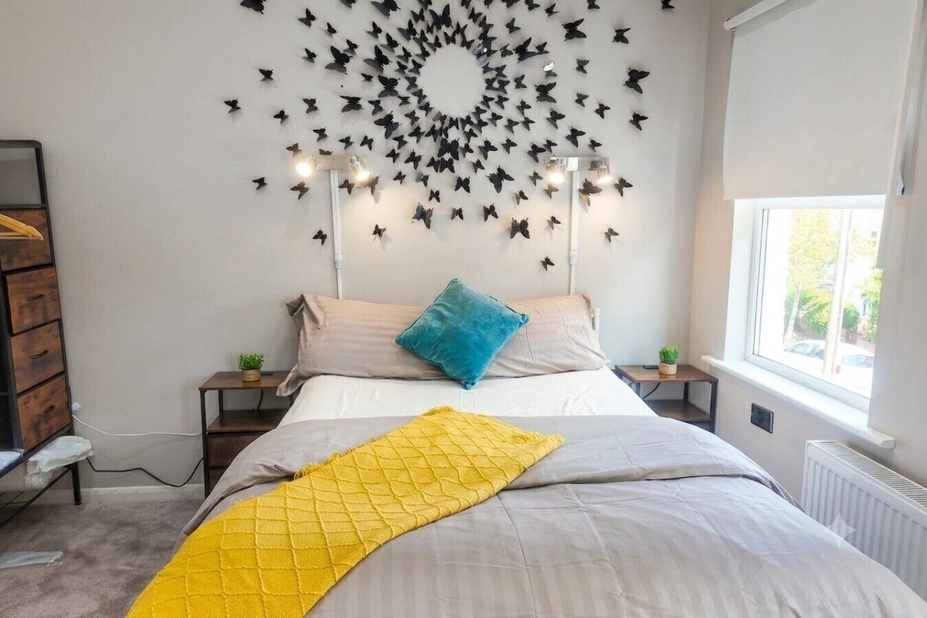 Une chambre à coucher comprenant un lit, un luminaire fixé au mur, une fenêtre et un radiateur.