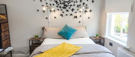 Une chambre à coucher comprenant un lit, un luminaire fixé au mur, une fenêtre et un radiateur.