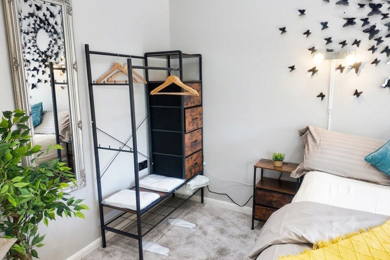 A bedroom with a bed, a wardrobe with a mirror, a hanging shelf, and a wall with butterfly decals.