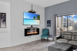 A modern living room with a flat-screen TV, a fireplace, teal chairs, and a leather sofa. - Cozy 2-bedroom condo in welcoming Kissimmee with AC and gym access (Kissimmee)