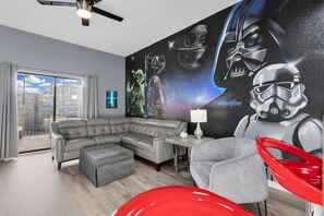 Ein modernes Wohnzimmer mit einer Eckcouch, einem roten Sessel, einem kleinen Tisch mit einer Lampe und einer Wandmalerei zum Thema Star Wars.