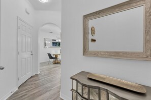 Ein Flur mit Holzboden, einer weißen Tür, einem Spiegel mit Beleuchtung und einem kleinen Tisch mit Tablett.