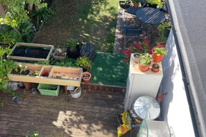 Eine Holzterrasse mit erhöhten Blumenbeeten, Topfpflanzen und einem kleinen Tisch.