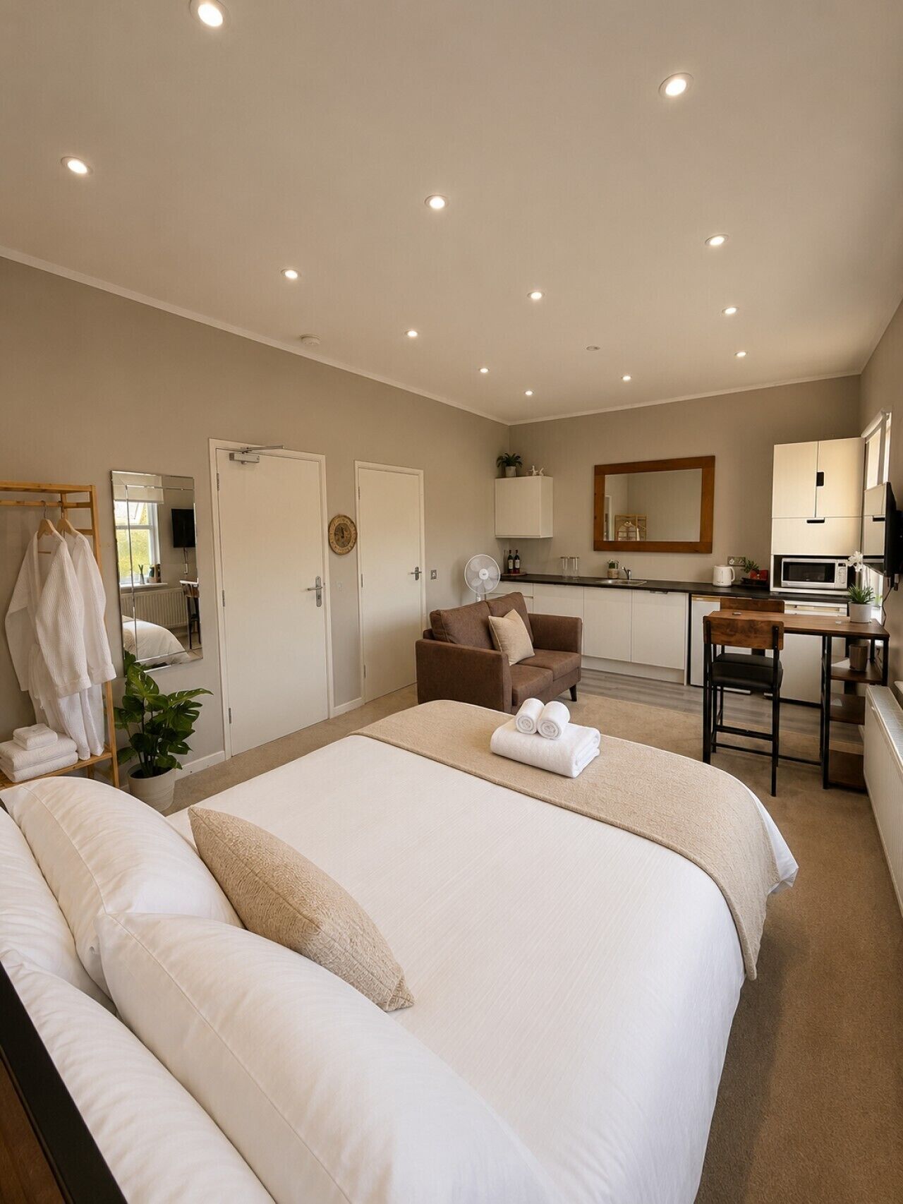 A hotel room with a large bed, a sitting area with a sofa, a desk with a chair, a mirror, and a kitchenette.