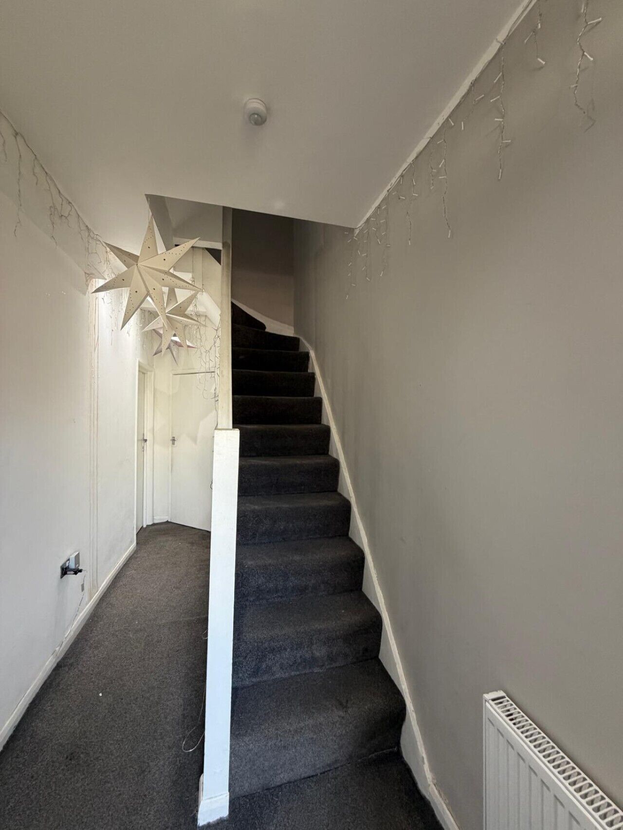 Een trap met beklede treden die uitkomt op een plateau, een witte deur en een plafondlamp.