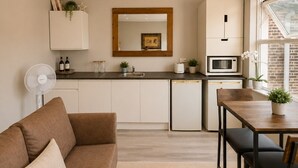 A modern kitchen with a dining area, a sofa, and a fan. - Double Bedroom with Kitchenette (London)