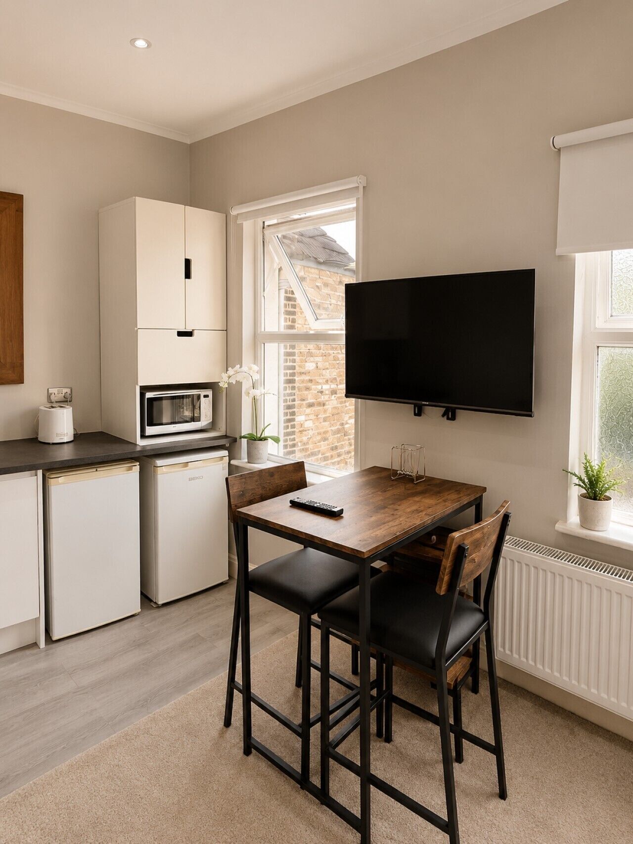 Une cuisine moderne avec un coin repas, un téléviseur à écran plat fixé au mur et une fenêtre laissant entrer la lumière naturelle.