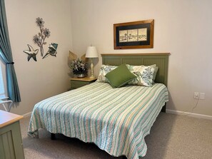 A bedroom with a bed, a nightstand, a lamp, a framed picture, and wall decorations. - GOLF, BEACH & POOL - RENOVATED 3BR Waterview Condo on Golf Course - RELAX! (Sunset Beach)