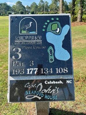 Un panneau indiquant un club de golf, avec son logo, le numéro du parcours et son adresse.