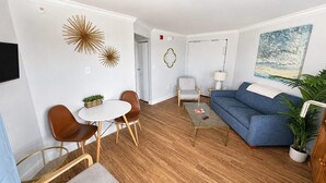 A modern living room with a blue sofa, a coffee table, and a dining area with chairs and a small table. - Captivating Oceanview Balcony & Resort Pools (Myrtle Beach)