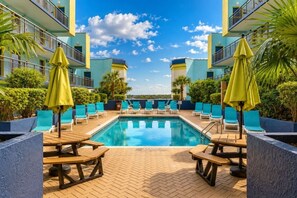 A pool area with lounge chairs and umbrellas, surrounded by greenery and a clear sky. - Captivating Oceanview Balcony & Resort Pools (Myrtle Beach)