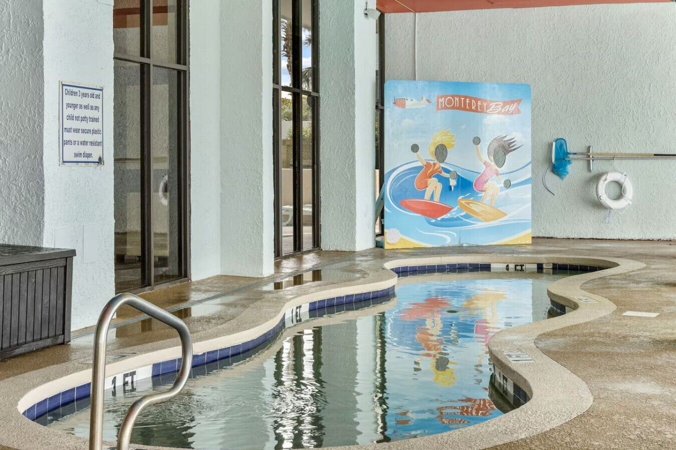 An indoor pool with a mural, a lifeguard stand, and a sign indicating pool rules.