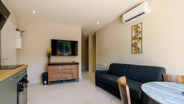 A modern living room with a flat-screen TV, a sofa, a dining table, and a decorative wall piece. - Opal 11 Apartment (Cannes)