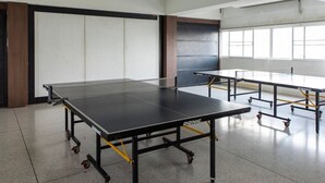 Una habitación con mesa de ping pong, otra mesa y un ventanal grande.