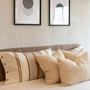 A sofa with striped and solid pillows, framed artwork on the wall, and a textured wall. - 49sqm 1BR in Thonglor, pool and workspace (Watthana)