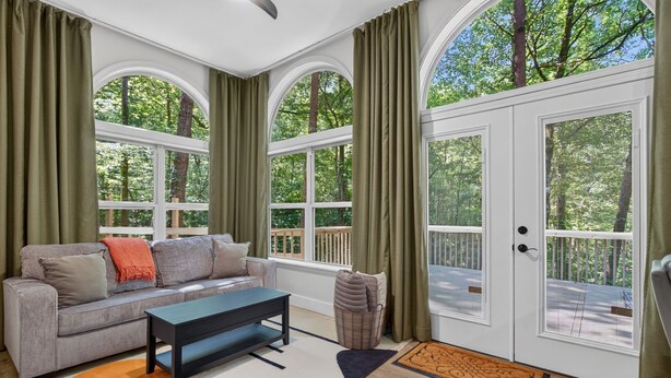 A living room with a sofa, coffee table, and large windows with curtains. - Gem of the Mountain -Cozy Cabin Retreat Near Helen (Sautee Nacoochee)