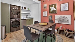 A modern kitchen with a built-in washer and dryer, a dining area with a wooden table and chairs, and a wall decorated with framed wildlife art. - Gem of the Mountain -Cozy Cabin Retreat Near Helen (Sautee Nacoochee)
