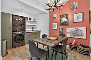 A modern kitchen with a built-in washer and dryer, a dining area with a wooden table and chairs, and a wall decorated with framed wildlife art. - Gem of the Mountain -Cozy Cabin Retreat Near Helen (Sautee Nacoochee)