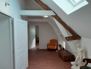 An interior with a sloped ceiling, a door, an orange chair, a statue, and a wooden bench. - Ancienne longère de caractère rénovée à 40mn du Mans (Saint-Denis-d'Orques)