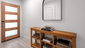 A hallway with a wooden console table, books, a bowl, and a mirror. - Vaulted Ceilings Home with 2,000-Book Library (Austin)