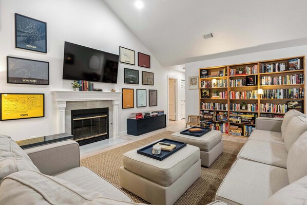 A modern living room with a fireplace, a large flat-screen TV, a bookshelf, and a sofa. - Dog-Friendly Home: 2,000- Books & Board Games (Austin)