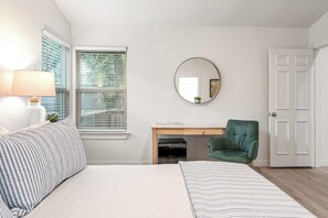 Ein Schlafzimmer mit einem Bett, einem Schreibtisch, einem Stuhl, einem Spiegel und einer Tür.
