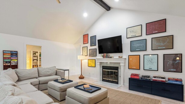A modern living room with a sectional sofa, a fireplace, a flat-screen TV, and a bookshelf. - Vaulted Ceilings Home with 2,000-Book Library (Austin)