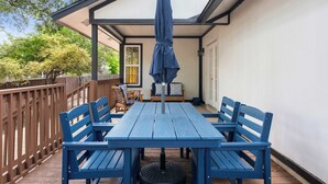 A covered patio with a blue table and chairs, a wooden fence, and a view of the house. - Vaulted Ceilings Home with 2,000-Book Library (Austin)