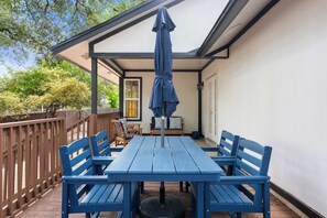 Eine überdachte Terrasse mit einem blauen Tisch und Stühlen, einem Holzzaun und Blick auf das Haus.