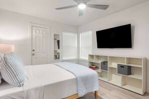 Ein Schlafzimmer mit Bett, Deckenventilator, Wand-TV und eingebauten Stauraumelementen.