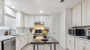 A modern kitchen with white cabinets, stainless steel appliances, and a central island. - Vaulted Ceilings Home with 2,000-Book Library (Austin)