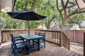 A wooden deck with a table and chairs, a black umbrella, and a wooden fence. - Dog-Friendly Home: 2,000- Books & Board Games (Austin)
