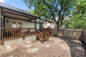 Ein Wohnhaus mit überdachter Veranda, Holzterrasse und eingezäunter Garten.