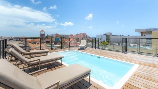 Una piscina sul tetto con poltrone relax, cielo sereno e edifici in lontananza.