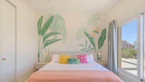 Una camera da letto con un letto, un comodino, un affresco al muro e una grande finestra.