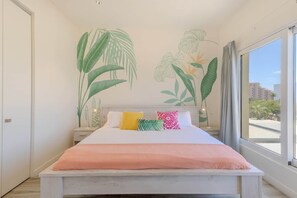 Ein Schlafzimmer mit einem Bett, einem Nachttisch, einer Wandmalerei und einem großen Fenster.